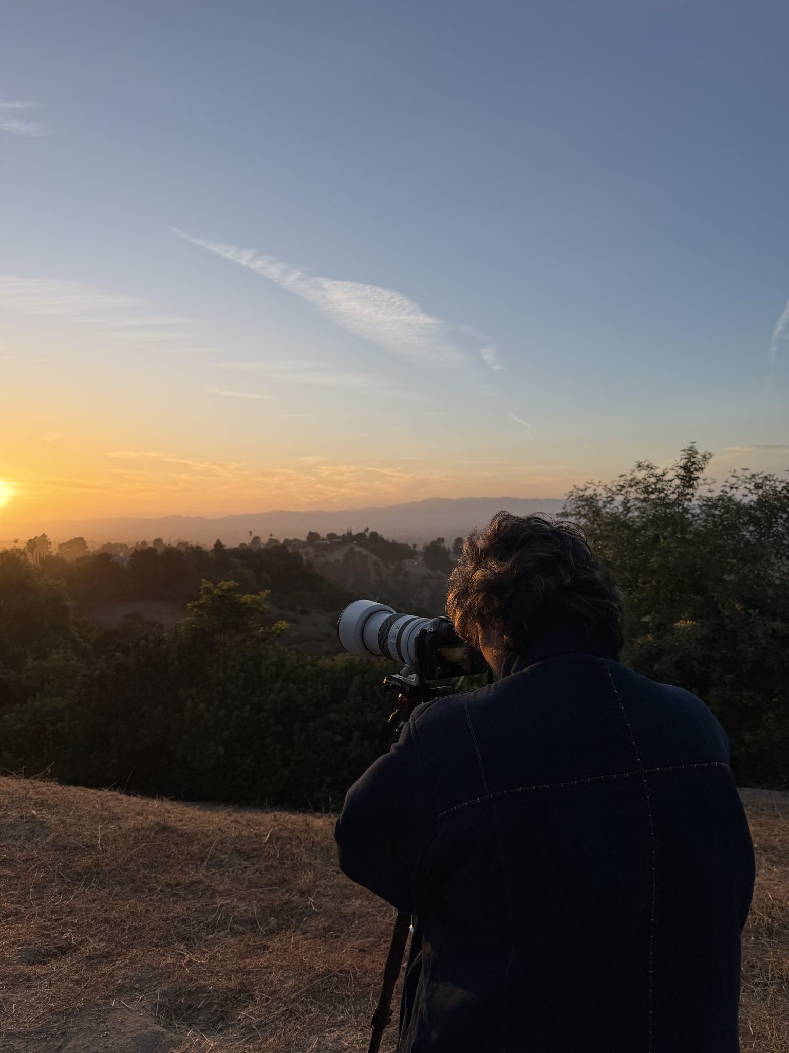 A photographer silhouetted against the sunset, long lens on a tripod.