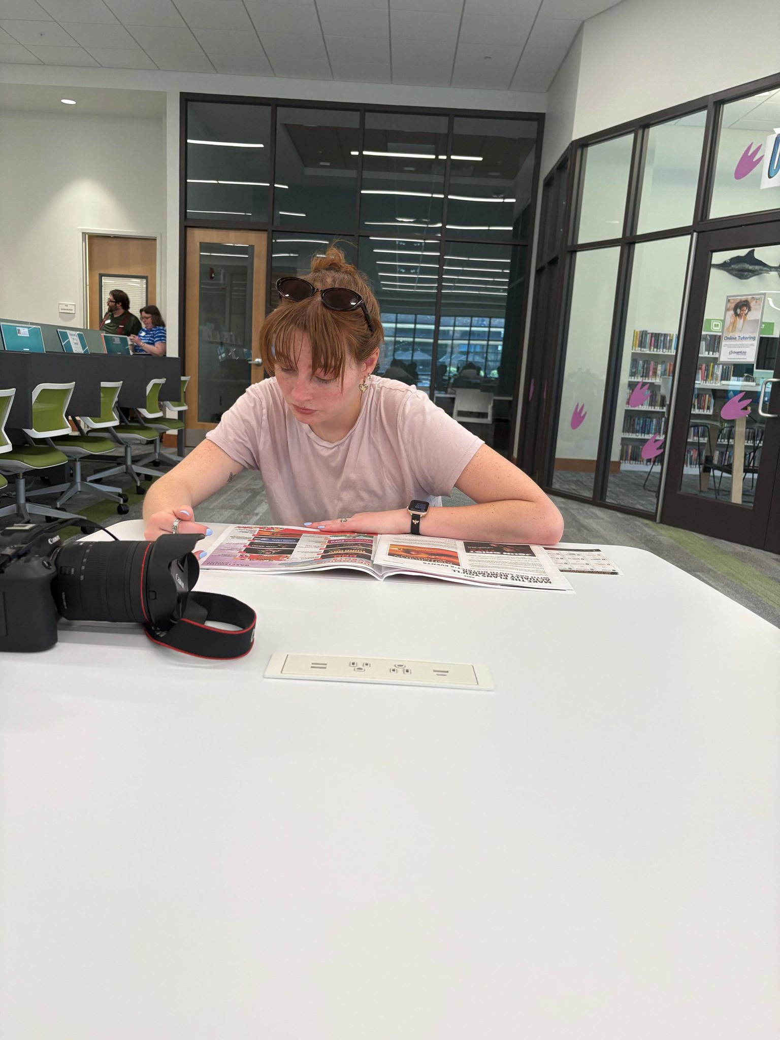 A fellow takes notes at a library table beside a camera.